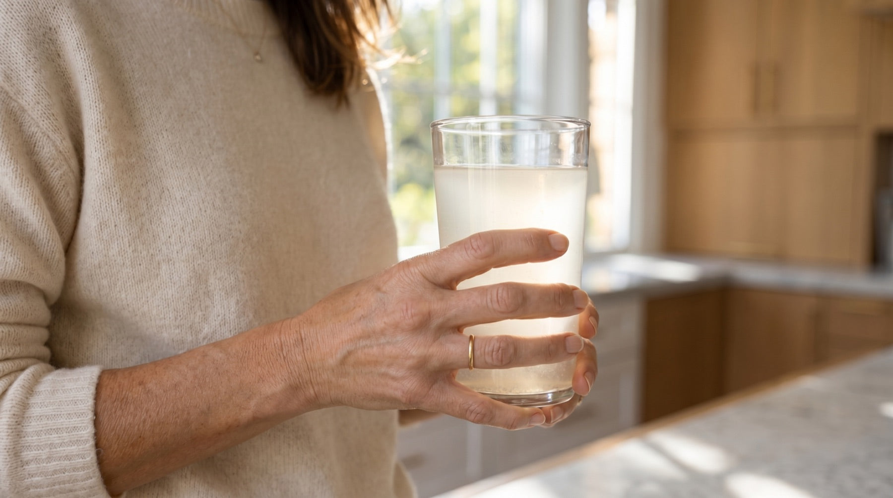 Hands holding a glass of cloudy lemon creatine water in the afternoon.