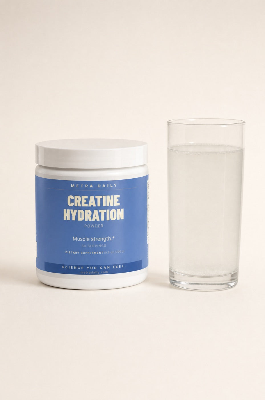 The Metra Creatine Hydration tub in Lemon beside a glass of the cloudy mixed drink.